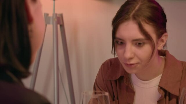 Two women meet in a cafe, with a close-up on one. They share stories and smile warmly, enjoying each other's company. Sipping white wine, they clink glasses in a joyful moment.