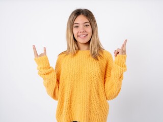 Beautiful teenager girl wearing knitted yellow sweater makes rock n roll sign looks self confident and cheerful enjoys cool music at party. Body language concept.