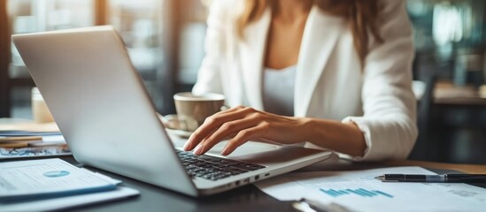Woman's hand typing on a laptop with a cup of coffee in front of her on a desk.