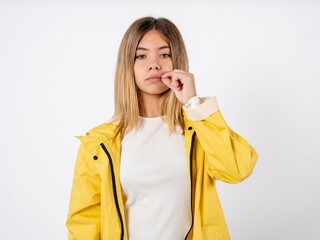 Beautiful teenager girl wearing yellow raincoat mouth and lips shut as zip with fingers. Secret and...
