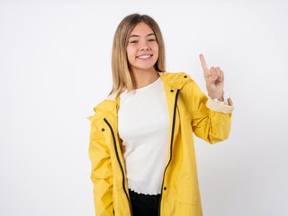 Beautiful teenager girl wearing yellow raincoat showing and pointing up with finger number one...