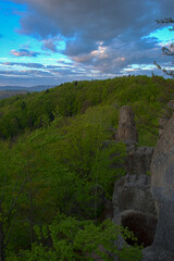 Forest and rocks at sunrise on hill and mountains in low clouds at sunrise in spring in Ukraine. Colorful landscape with forests in fog, sun rays, sky, forest at dawn. HDR style.