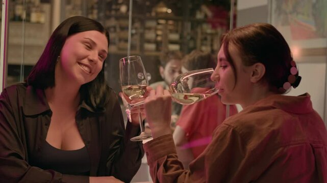Two best friends reunite in a cafe early in the morning, sitting with glasses of white wine. They engage in lively discussion after time apart. Both wear casual shirts, reflecting their relaxed style.