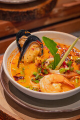 Close up, Spicy seafood soup with herbs in bowl, place on wooden slab. Thai dish called 
