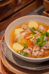 High angle, Clear soup with dried squid, dried shrimp, minced pork and chinese cabbage in bowl, place on wooden slab. Thai dish called "TOM JUED"