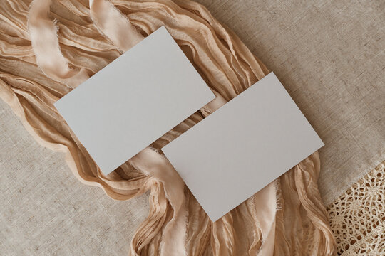 Blank white paper cards mock up on a beige fabric background with ribbons. Aesthetic minimalistic business brand template, wedding invitation design, greeting card, copy space