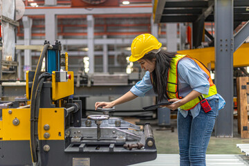 Female mechanical engineer in safety suit checking or inspecting a machine in metal sheet...