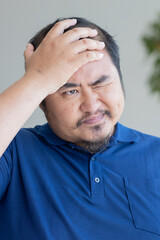 Obraz premium Serious Asian middle aged man with negative facial expression, upset unhappy mid age old real man with failed mood, slapping his head with upset emotion, Frustration and disappointment
