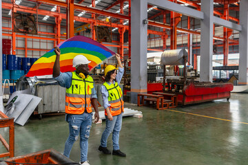 Two mechanical engineers from different ethnicities express their pride for LGBT by showing a ribbon flag in a metal sheet factory. Human rights and gender equality in industry