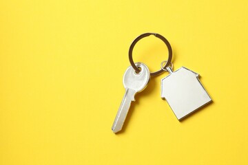 Metallic key with keychain in shape of house on color background