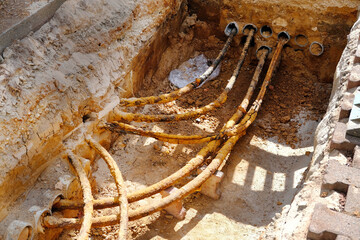 An excavated pit reveals water pipes and electrical cables, showcasing underground infrastructure...