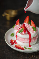 Słodka beza Pavlowa z truskawkami i kremem truskawkowym na ciemnym tle. © Dorota