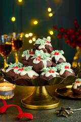 Chocolate profiteroles decorated with white chocolate and creamy holly on a gold stand. Christmas festive dessert