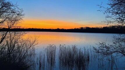 Serene sunset over a tranquil lake, surrounded by silhouettes of trees.