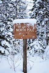 Sign marking the North Pole surrounded by snowy trees during winter