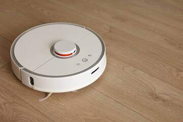 Top view of white wireless autonomous robotic vacuum cleaner on wooden floor. Smart cleaning...