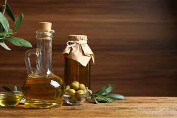 Bottles of fresh olive oil and olives with leaves on wooden background