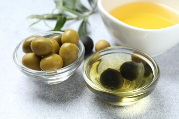 Bowl of fresh olive oil and olives with leaves on wooden background