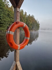 A bright orange life ring hanging from a wooden support, set against a tranquil lakeside scene
