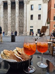 Two glasses of orange spritz aperol drink cocktail and tasty sandwiches on table outdoors with the city in the background