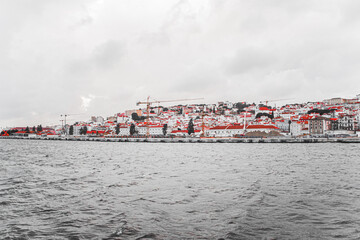 Scenic Urban Landscape Featuring Red-Tiled Rooftops and Cranes Overlooking a Tranquil Waterfront on...