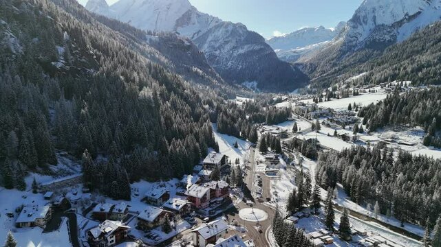 Canazei, Italy: Aerial view of ski resort in snowy Dolomites. Charming town landscape with chalets and hotels surrounded by snow-capped peaks, sunny day, clear blue sky
