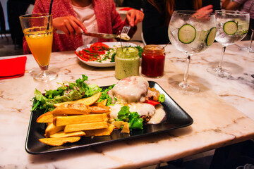 Gourmet Dining Experience with Sizzling Chicken Dish and Fresh Salad on Marble Table with Friends Enjoying Drinks