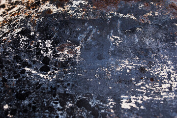 a surface with a texture resembling rust or burnt metal. It has dark and light patches, with the dark areas appearing as black or dark blue and the light areas appearing as white or light brown.