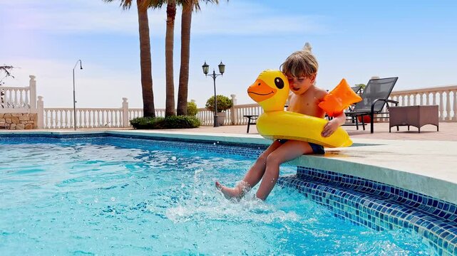 Boy kid splashes with legs at pool in floaty, under a sunny sky