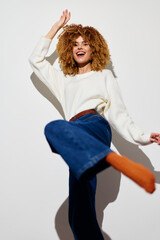 Happy woman dancing in casual outfit, beige sweater, blue jeans, joyful expression, white background, capturing carefree spirit and energy, perfect for lifestyle concepts