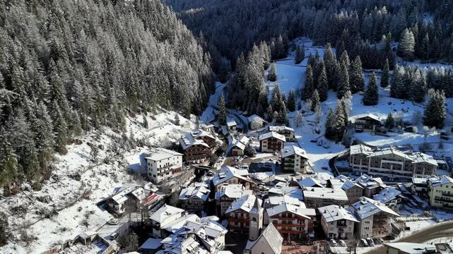Canazei, Italy: Aerial view of ski resort in snowy Dolomites. Charming town landscape with chalets and hotels surrounded by snow-capped peaks, sunny day, clear blue sky
