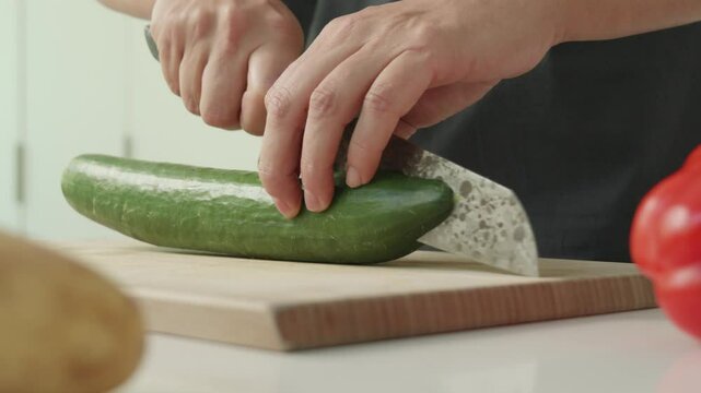 Slow-motion shot of a cucumber being sliced lengthwise on a wooden cutting board, with the two halves rolling open.