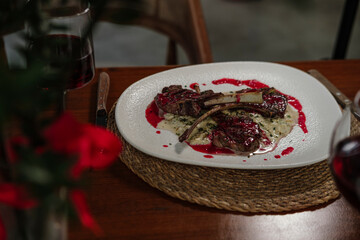 lamb chop stick grilled with red cherry sauce setted with porridge and topped with seasonal herbs, served with red wine in restaurant on wooden table