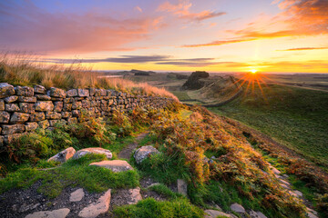 Vibrant summer sunrise at Hadrians Wall overlooking Cuddy's Crags as the sun comes over the horizon. Northumberland, UK.