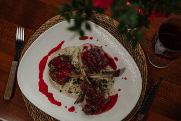 lamb chop stick grilled with red cherry sauce setted with porridge and topped with seasonal herbs, served with red wine in restaurant on wooden table