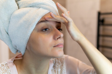 Young beautiful caucasian woman looking in the bathroom mirror at her eyes with dark circles under...