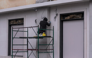 a worker on scaffolding plasters the wall of a building