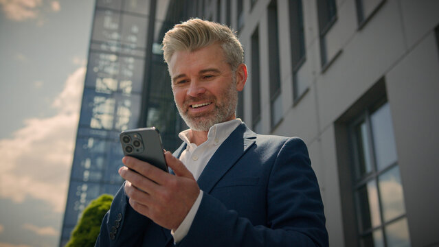 Caucasian senior middle aged employer mature happy businessman receive message offer opportunity retired business man read good news smartphone excited overjoyed celebrate mobile phone victory in city