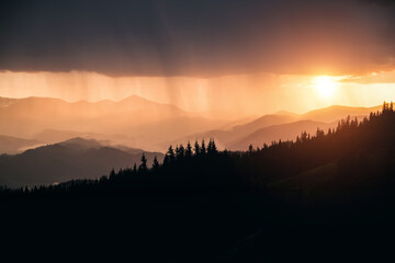 An incredible scene of a heavy downpour illuminated by the rays of the sun at sunset. Carpathian mountains, Ukraine, Europe.