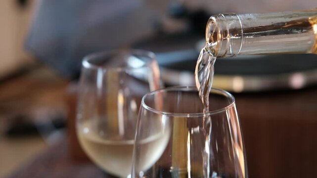 Pouring white wine into a glass from a bottle for cozy aperitif at home on the background of a record player