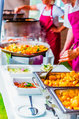 Colorful Outdoor Catering Buffet with Chefs in Red Aprons Serving Delicious Dishes at a Vibrant Event