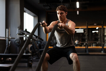 Healthy man athlete doing exercises with ropes, working out in gym, practicing hard and training his upper body