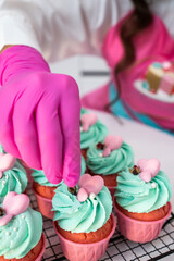 Cupcakes. Pink cupcakes with mint cream and pink decoration. Confectioner's hand in a pink glove. Decorate cupcakes