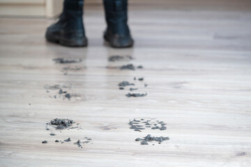 Mud Black boots next to muddy footprints on a polished wooden floor in living room. Uncleaned footprints on wooden floor after outdoor activity. Concept of dirty stains and house cleaning