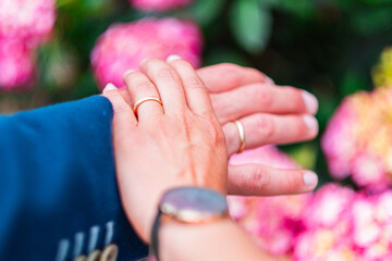 Close-Up of Couple's Hands with Wedding Rings Signifying Love and Commitment Amidst Pink Blossoms,...