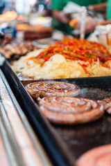 Close-Up of Sizzling Sausages and Colorful Grilled Vegetables on a Barbecue Grill at a Vibrant Outdoor Market or Festival