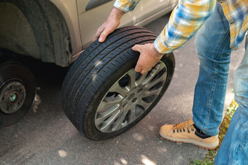 Man changing a tire beside a vehicle on a sunny day in a suburban area © Iryna