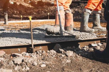 Construction workers mixing and pouring concrete at a construction site during daylight hours