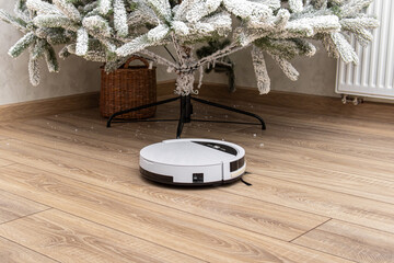 Artificial snow falling from the Christmas tree. Robot vacuum cleaner vacuums under the Christmas...