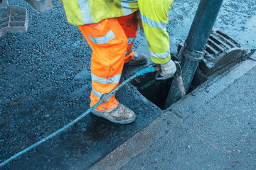 Worker in safety gear clears a drain at a publick road to prevent clogging and floding